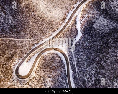 High-Angle-Luftaufnahme Drohne Bild auf der gebogenen Serpentin Straße durch die Bäume und Wald in Bergkette mit Weißer Schnee am Wintertag in der Nähe von Knja Stockfoto