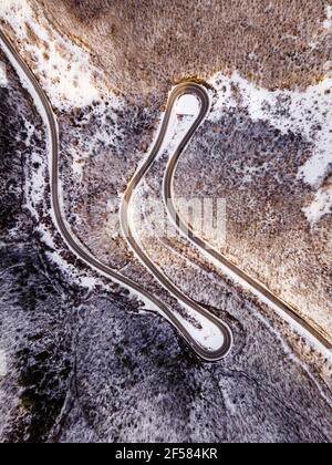 High-Angle-Luftaufnahme Drohne Bild auf der gebogenen Serpentin Straße durch die Bäume und Wald in Bergkette mit Weißer Schnee am Wintertag in der Nähe von Knja Stockfoto