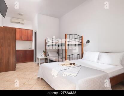 Weißes modernes Interieur von Familienanzug Schlafzimmer mit klassischen Doppelbett, Etagenbett mit Metalltreppen, hölzerne Küchenschränke in Einzelraum von kleinen Zimmer Stockfoto
