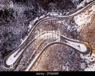 High-Angle-Luftaufnahme Drohne Bild auf der gebogenen Serpentin Straße durch die Bäume und Wald in Bergkette mit Weißer Schnee am Wintertag in der Nähe von Knja Stockfoto