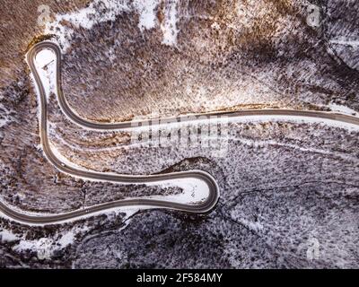 High-Angle-Luftaufnahme Drohne Bild auf der gebogenen Serpentin Straße durch die Bäume und Wald in Bergkette mit Weißer Schnee am Wintertag in der Nähe von Knja Stockfoto