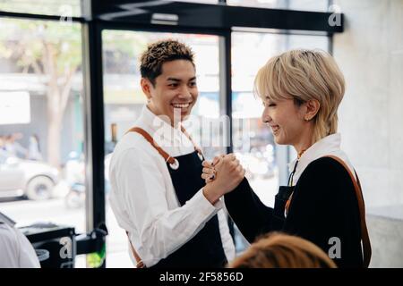 Fröhliche junge asiatische Mann und Frau Friseur trägt Schürze Uniform Im modernen Salon geben High-fünf einander auf feiern Erfolg des Salons Stockfoto