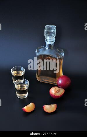 Eine Flasche und zwei Gläser Pflaumenlikör und geschnittene reife Früchte auf schwarzem Hintergrund. Nahaufnahme. Stockfoto