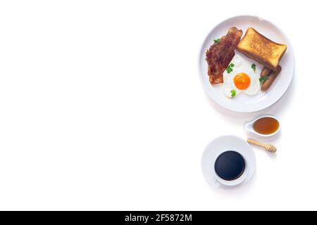 Frühstück, frischer Buttertoast, herzförmige Spiegeleier, Räucherwurst und gegrillter Speck serviert mit schwarzem Kaffee und Honig auf weißem Hintergrund, Top Stockfoto