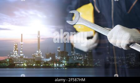 Doppelbelichtung des Mechanikers, der Stoffhandschuhe trägt, einen Schutzhelm (Schutzhelm) mit der Petrochemischen Raffinerie in der Nähe des Flusses in der Nacht hält. Stockfoto