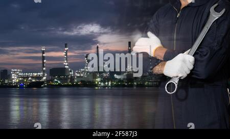 Doppelbelichtung des Mechanikers, der Stoffhandschuhe trägt, einen Schutzhelm (Schutzhelm) mit der Petrochemischen Raffinerie in der Nähe des Flusses in der Nacht hält. Stockfoto