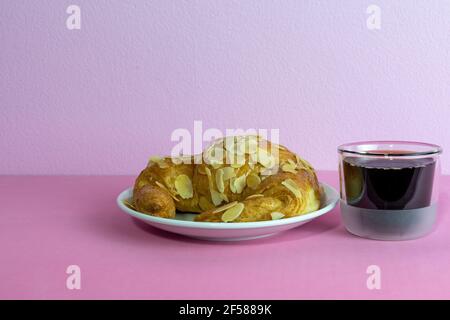 Mandelcroissant und eine Tasse Kaffee auf rosa Hintergrund. Stockfoto