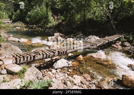 Holzbrücke über einen kleinen Gebirgsfluss in einem Frühlingswald. Sonniger Nachmittag. Ausflüge im Freien an einem freien Tag. Stockfoto