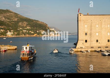 Boot, das den Hafen der Altstadt von Dubrovnik verlässt und bei Sonnenuntergang in Kroatien auf dem Balkan an der berühmten Festung St. Johannes vorbei fährt Stockfoto