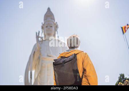 Männlicher Tourist auf dem Hintergrund der majestätischen Ansicht der Lady Buddha Statue der Bodhisattva der Barmherzigkeit, Vietnam. Weiße Ladybuddha Statue auf blauem Himmel Stockfoto