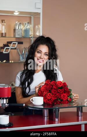 Liebenswürdicker Mitarbeiter des Schönheitssalons Empfang mit schönen Blumenstrauß rote Rosen. Lifestyle-Porträt von schönen Mädchen. Kleinunternehmen Nach Der Covid-19-Pandemie Stockfoto