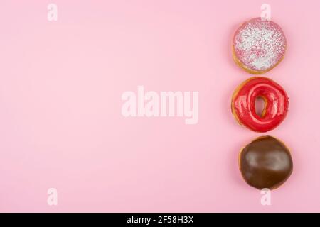 Die leckeren glasierten Donuts liegen auf einem rosa Hintergrund Stockfoto