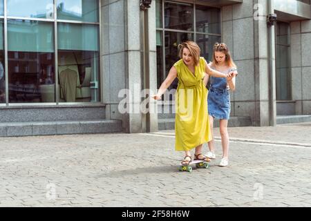 Mutter und Tochter verbringen Zeit miteinander. Tochter lehrt Mama auf einem Skateboard skaten. Aktiver Familienleben Stockfoto