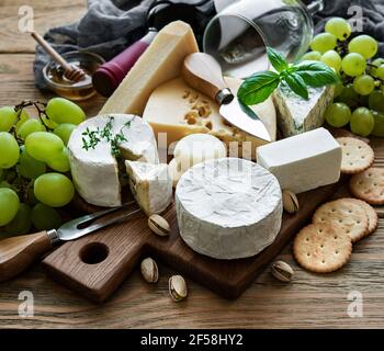 Verschiedene Arten von Käse, Trauben und Wein auf einem Holztisch Stockfoto