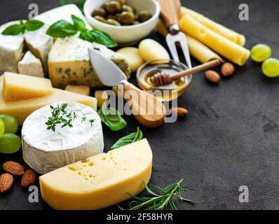 Verschiedene Käsesorten, Trauben, Honig und Snacks auf schwarzem Betongrund Stockfoto