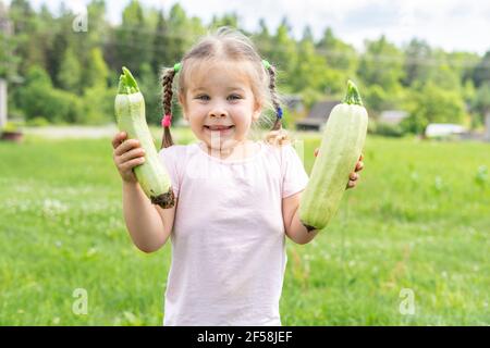 Fröhliches Kind Mädchen mit zwei frisch gepflückten Zucchini in der Dorf Stockfoto