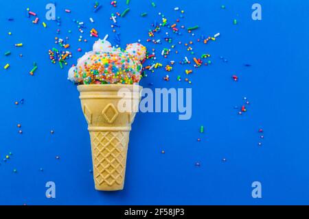 Eiskegel mit kleiner Tasse Kuchen mit Zuckerguss verziert Und runde Streuseln mit Streuseln verstreut und isoliert auf blau Hintergrund - Geburtstag BA Stockfoto
