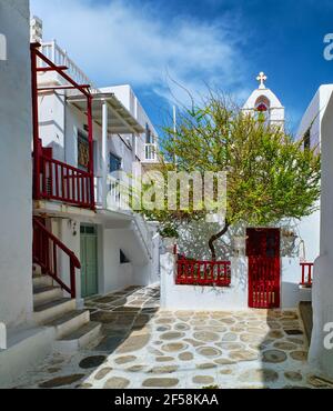 Schöne traditionelle enge gepflasterte Straßen, kleine Plätze der griechischen Inselstädte. Weiß getünchte Häuser. Kleine Kapelle und Olivenbaum. Mykonos, Griechenland. Stockfoto