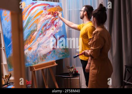 Ein paar Künstler sprechen und malen in ihrer Kunstwerkstatt. Moderne Kunst malen auf Leinwand, kreative, zeitgenössische und erfolgreiche bildende Kunst Künstler Zeichnung Meisterwerk Stockfoto