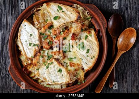 Tartiflette, French Potato, Bacon und Käse Auflauf in einer Tonschale auf einem dunklen Holztisch mit Löffel, flach legen Stockfoto