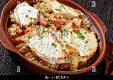 Tartiflette, French Potato, Bacon und Käseauflauf in einer Tonschale auf einem dunklen Holztisch, Nahaufnahme, französische Küche Stockfoto