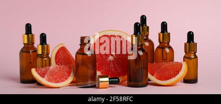 Tropfflaschen mit Öl und Grapefruitscheiben auf rosa Hintergrund Stockfoto