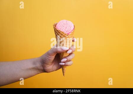 Eis in Waffelbecher in weiblicher Hand auf gelb Hintergrund Stockfoto