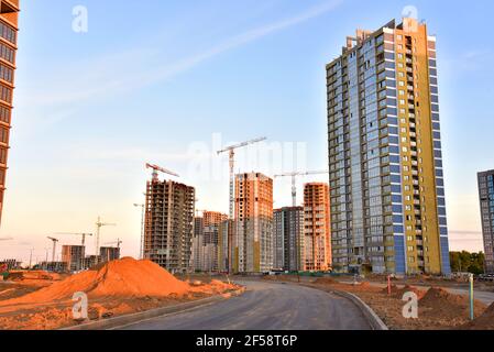 Blick auf die große Baustelle mit Turmdrehkranen und Gebäuden im Sonnenuntergangshintergrund. Mehrstöckiges Wohngebäude wird gebaut Stockfoto