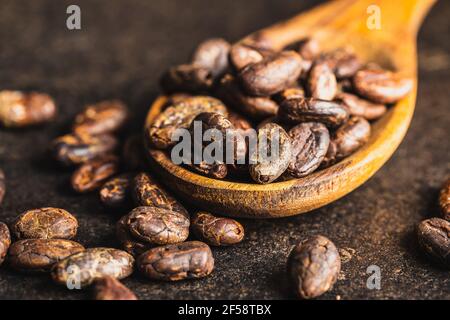 Geröstete Kakaobohnen in Holzlöffel auf schwarzem Tisch. Stockfoto