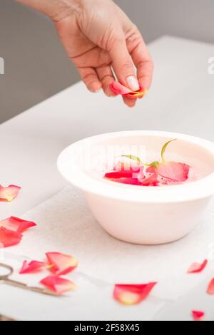 Die weiblichen Hände der Kosmetikerin bereiten das Maniküre-Bad mit Rot und Rosa vor rosenblüten auf dem Tisch im Spa Stockfoto