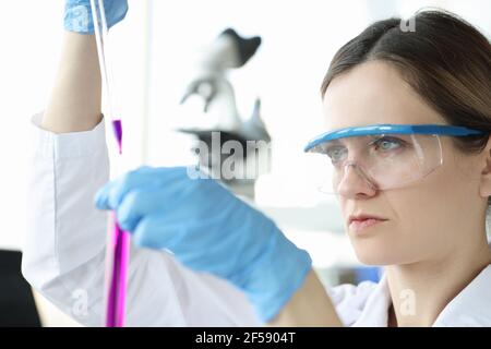 Frau Chemikerin in Schutzgläsern tropft rosa Flüssigkeit in Test Schlauch Stockfoto