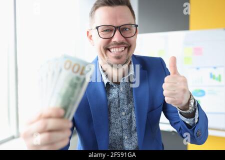 Geschäftsmann hält Dollar in den Händen und zeigt Daumen nach oben Stockfoto