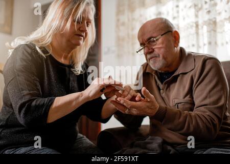 Ältere Frau überprüft den Blutzucker ihres diabetischen Mannes bei Zu Hause Stockfoto