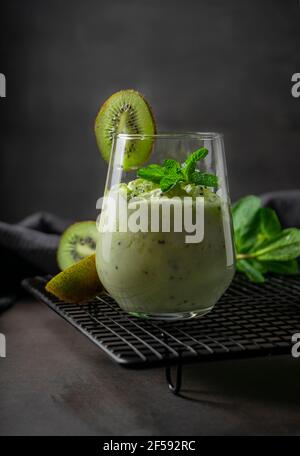 Tropischer Smoothie aus reifen Kiwi. Richtige Ernährung, kalorienarmer gesunder Fruchtdrink. Auf dunklem Hintergrund mit Minze-Zweige Stockfoto