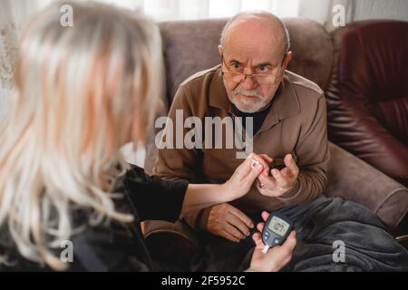 Ältere Frau überprüft den Blutzucker ihres diabetischen Mannes bei Zu Hause Stockfoto