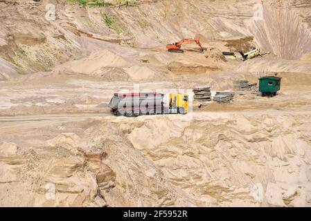 LKW mit Kipper Sattelauflieger transportiert Sand aus dem Steinbruch. Muldenkipper und Bagger arbeiten in Tagebau. Sand und Kies werden ausgegraben Stockfoto