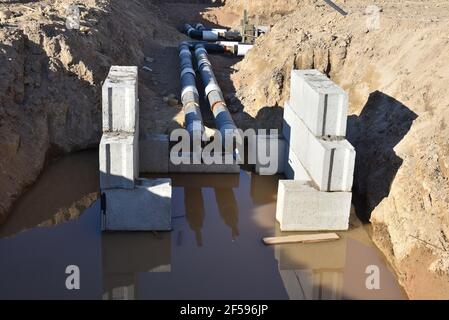 Verlegung von Heizrohren in einem Graben auf der Baustelle. Installation von unterirdischen Sturmsystemen für die Wasserleitung und die Sanitärabwasserkanäle Kaltes und warmes Wasser, Heizung Stockfoto