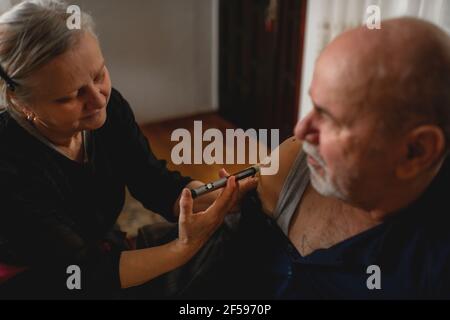 Ältere Frau, die ihrem diabetischen Mann zu Hause Insulin gibt Stockfoto