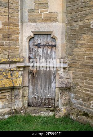 Eine verwitterte und verfaulte Holztür in einer Steinmauer mit Vorhängeschloss und Kettenschutz. Stockfoto