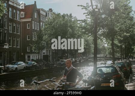 AMSTERDAM, NIEDERLANDE - Jul 01, 2019: Eine horizontale Aufnahme eines männlichen Touristen, der an einem sonnigen Kanal von Amsterdam entlang geht Stockfoto