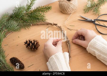 Frau macht einen weihnachtskranz mit Tannen und Zapfen auf einem Holztisch. Stockfoto