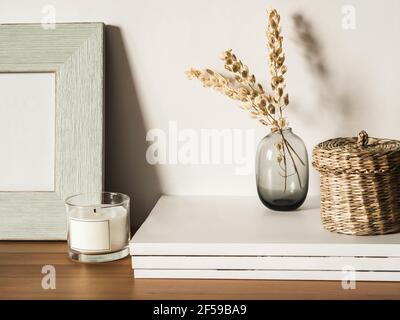 Home Stillleben von trockenen Blumen in Vase, Strohdose, Glaskerze und Zeitschriften auf Holztisch. Speicherplatz kopieren. Vorderansicht Stockfoto