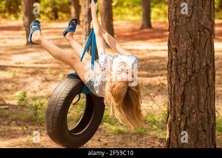 Nettes kleines Mädchen schwingt auf Rad an großen Baum im Herbstwald befestigt. Stockfoto