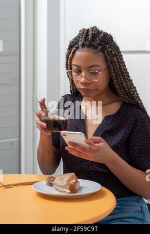 Frau beim Frühstück in einer modernen weißen Küche beim Schauen Auf dem Handy Stockfoto