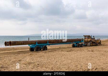 CAT Caterpillar D7H Series II Transport von großen Rohren auf Anhänger entlang Strand für Strand Nachschub Arbeit in Bournemouth und Poole Beaches, Dorset UK Stockfoto