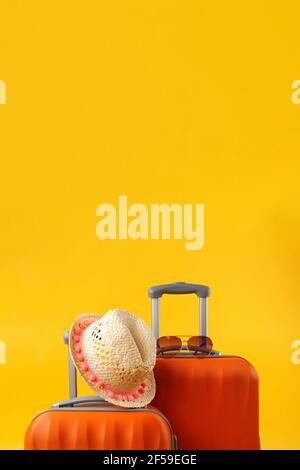 Sommerzeitkonzept. Nahaufnahme von zwei Reisetaschen Koffer, Strohhut und Sonnenbrille auf gelbem Hintergrund mit Kopierraum. Stockfoto