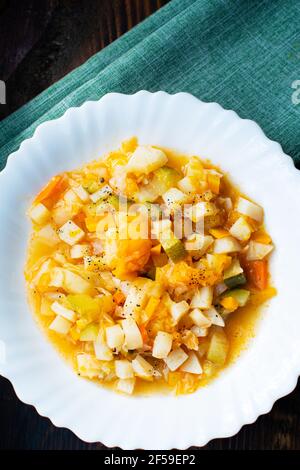 Mischen Sie das geschmorte Gemüse auf einem weißen Teller im Café. Gemüseeintopf in Tomatensauce. Gekochte vegane oder vegetarische Speisen. Stockfoto