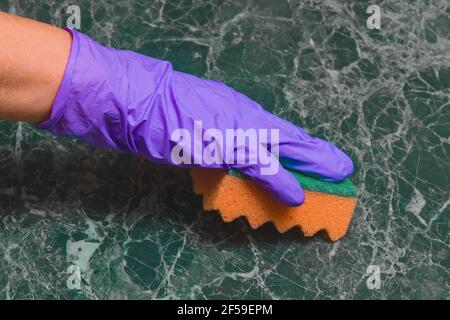 Hausfrau Frau Hand in Gummi Haushaltshandschuh wäscht grünen Marmor Oberfläche mit einem Schwamm. Stockfoto