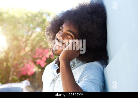 Nahaufnahme des lachenden Afro-Mannes, der sich an die Wand lehnt Sprechen auf dem Handy Stockfoto