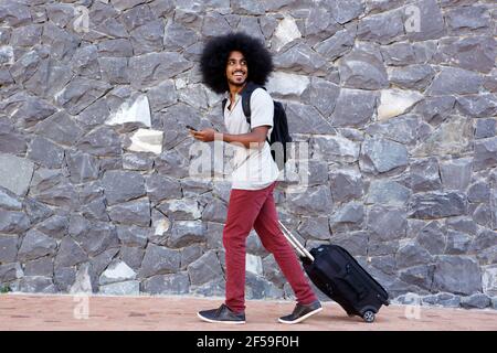 In voller Länge Porträt von lächelndem Reisemann mit Telefon und Taschen laufen draußen Stockfoto